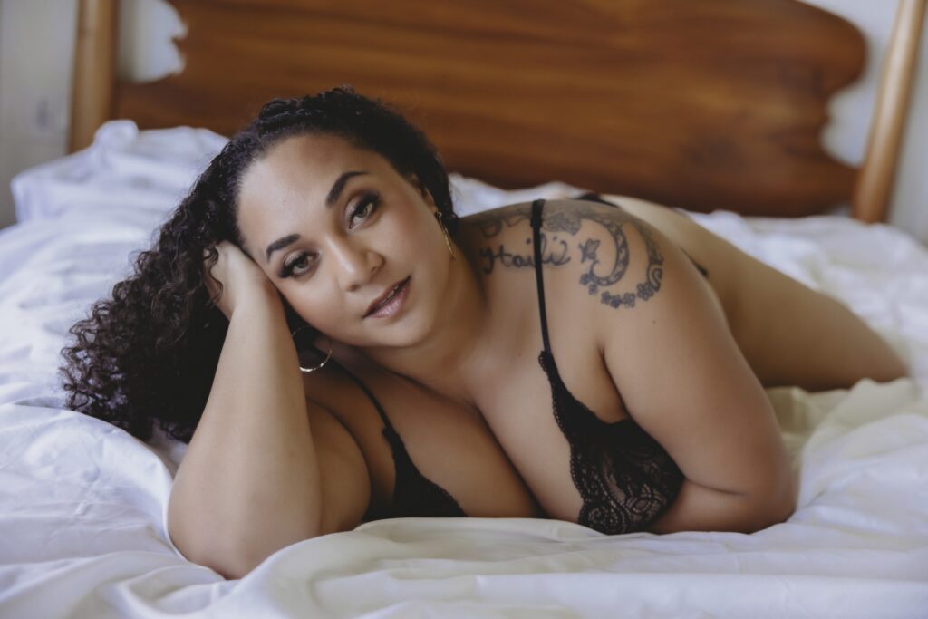 Woman laying on bed in black lace lingerie, looking at camera – women's portrait photography Hawaii.