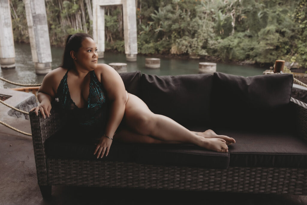 A woman looking out at the water, while lounging on outdoor sofa in lingerie, captured in soft natural light. This image highlights relaxed elegance and confidence in a tropical setting, showcasing women's portrait photography Hawaii.