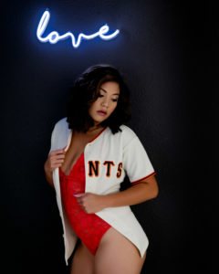 Woman in sports jersey under neon love sign - boudoir session