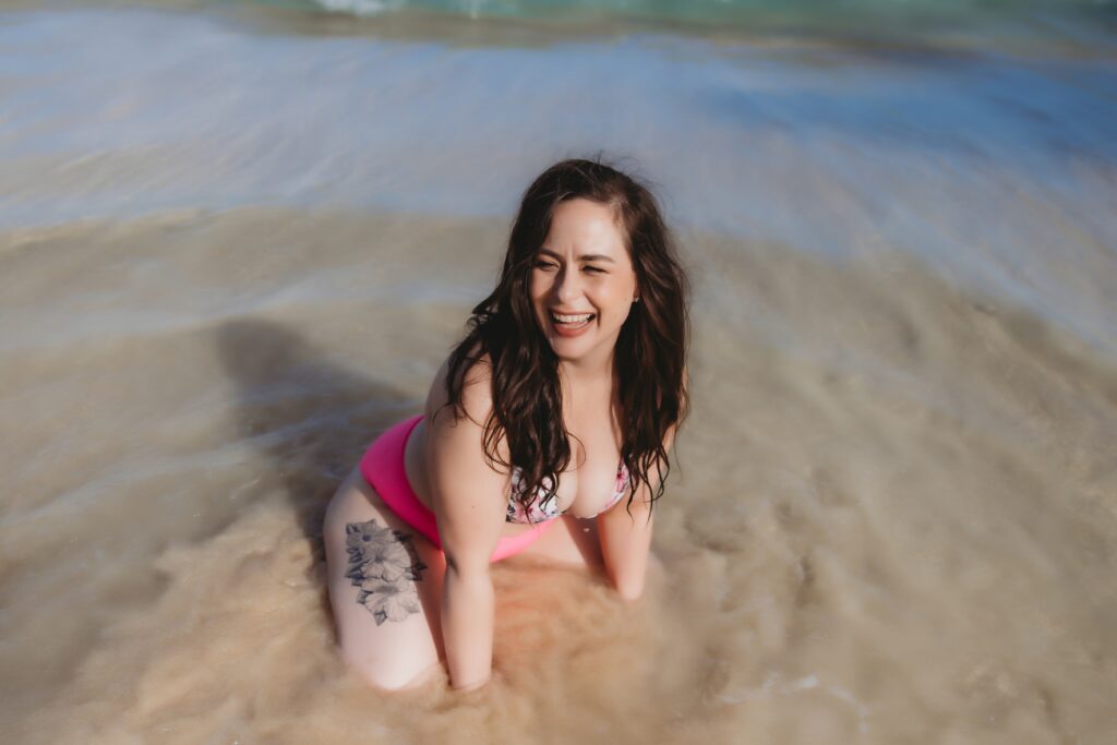women in pink bikini at the beach in Oahu smiling and playing in the ocean for Oahu Boudoir session