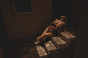 Moody luxury boudoir portrait of a woman reclining on marble steps in dramatic light during a Hawaii boudoir photography session.